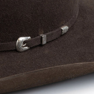 Brown hat with a decorative band and buckle on a light gray background