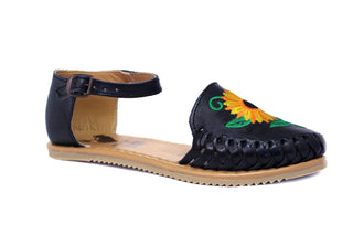 Side view of a black colored leather closed toe sandal with an ankle buckle and a sunflower embroidery on the face