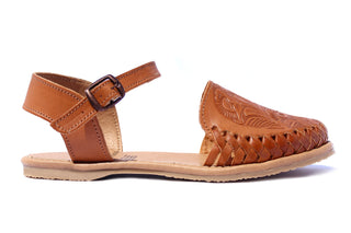 Side view of a honey colored leather closed toe sandal with an ankle buckle and a floral imprint on the face