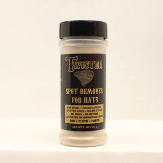 A bottle of Twister Spot Remover for Hats, featuring a black cap and a black label with gold lettering, containing a light beige powder, set against a plain off-white background.