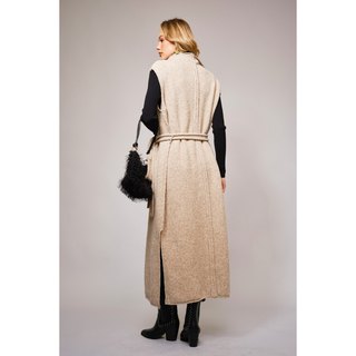 back view of long beige knit vest with waist tie over a black turtleneck and pants, styled in modern western fashion