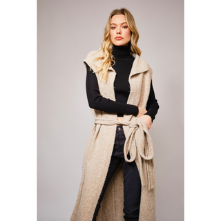 long beige knit vest with waist tie over a black turtleneck and pants, styled in modern western fashion