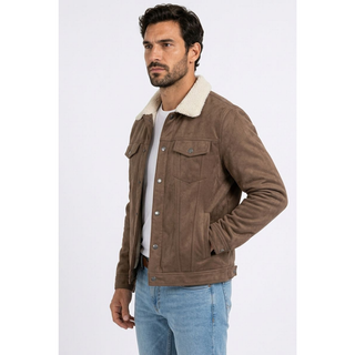 A man wearing a brown faux suede jacket with a cream sherpa collar, styled over a white t-shirt and light blue jeans, photographed against a light gray studio background.