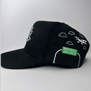 Left side of JG Hats Charros de Jalisco cap with airplane, clouds, and 'Bienvenidos a Jalisco' embroidery
