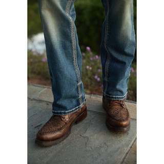 Close-up of the lower leg of Platini Holt boot cut jeans paired with brown woven leather shoes.